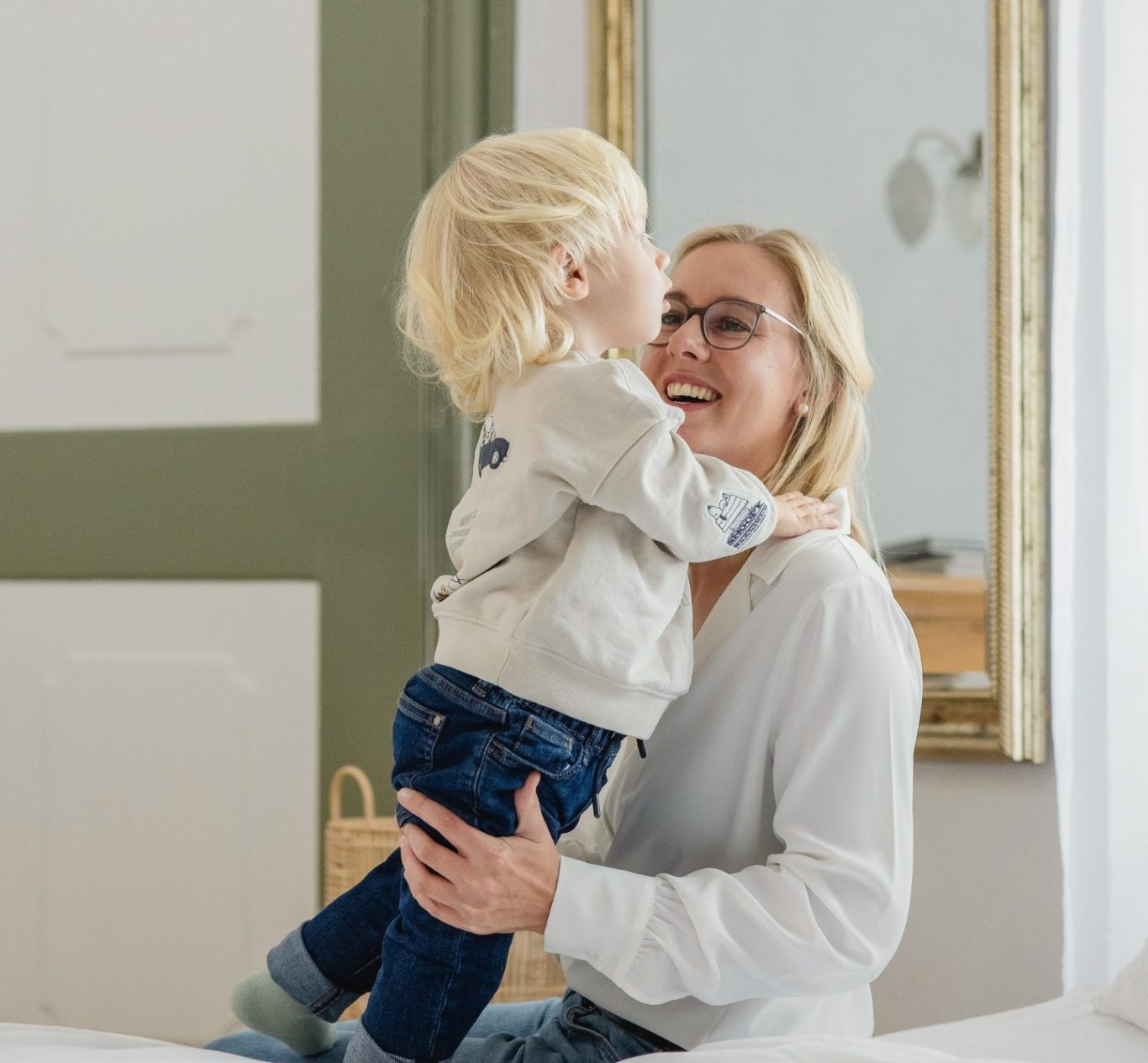 Familienberatung, Stillberatung, Schlafberatung, Beikostberatung Ein lachender Junge umarmt seine Mutter, die glücklich auf einem Bett sitzt.