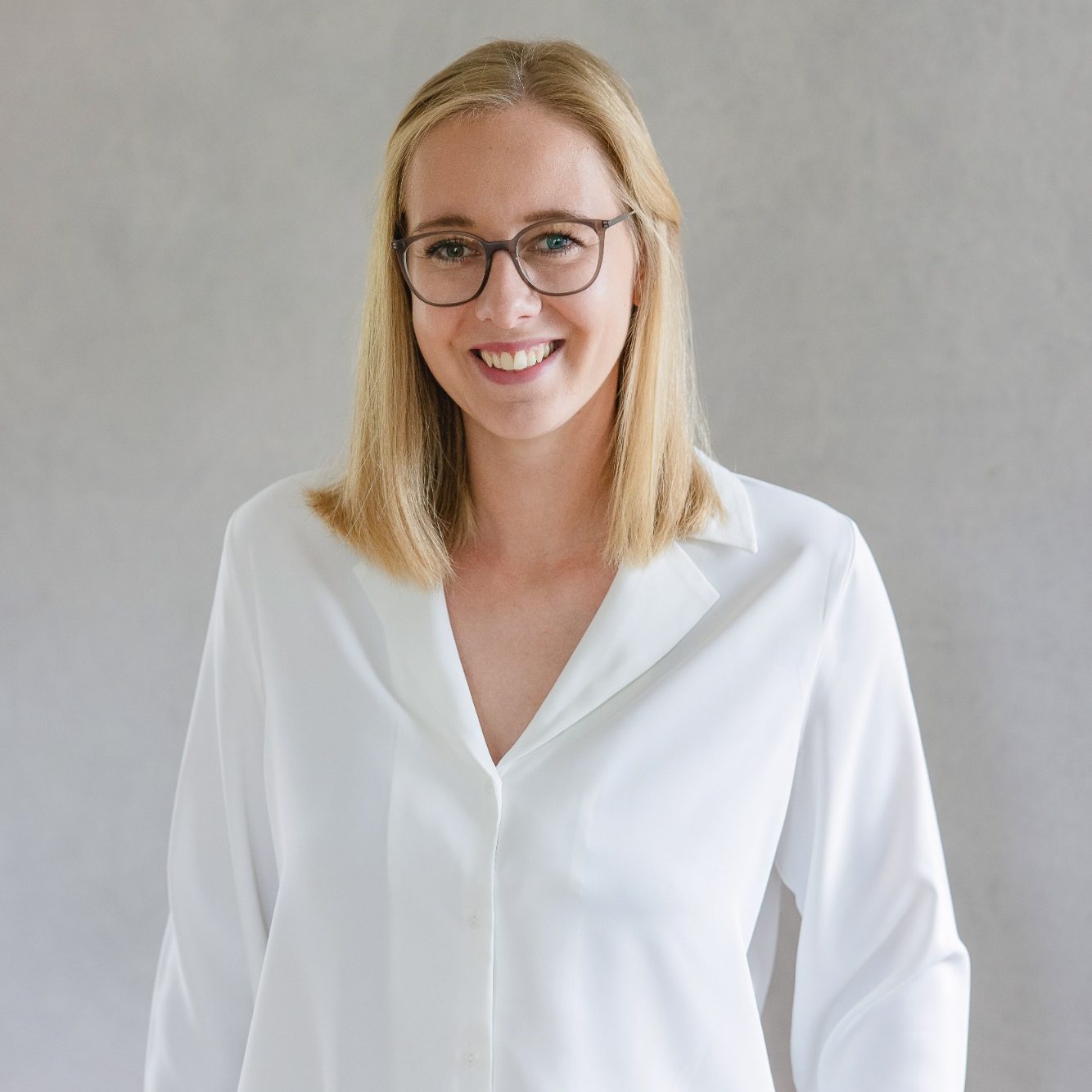 Magdalena Beckers Bidungsorientierte Familienbegleiterin Junge Frau mit blonden Haaren und Brille, trägt ein weißes Hemd und lächelt.